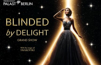 Eine Frau im eleganten Abendkleid steht zentral im Lichtstrahl, umgeben von Sternen. Schirmt mit der rechten Hand ihre Augen ab, als wäre sie geblendet. In goldener Schrift steht groß Blinded by Delight, Querformat.