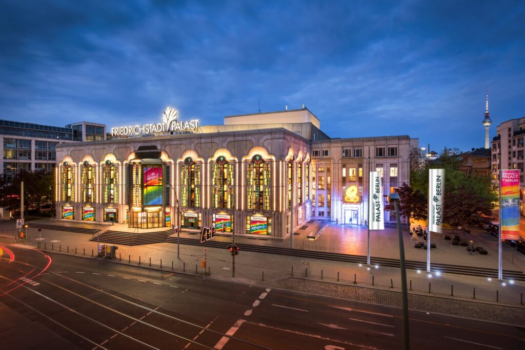Beleuchteter Friedrichstadt-Palast in Berlin mit bunten Lichtern und Werbebannern, umgeben von Straßenverkehr