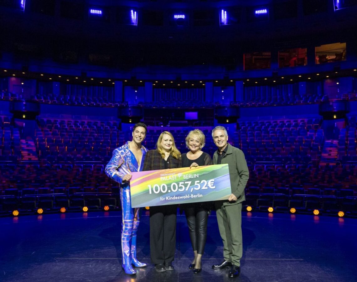 Vier Personen auf der Bühne des leeren Friedrichstadt-Palasts halten einen Spendenscheck über 100.057,52 € für Kindeswohl-Berlin. Von links nach rechts: Intendant Berndt Schmidt, Susanne Ferjani (Geschäftsführung Kindeswohl-Berlin), Natascha Lecki (Mitglied der Intendanz und Direktorin Marketing, Sales & PR) und Julian David, Solist der Show BLINDED by DELIGHT.