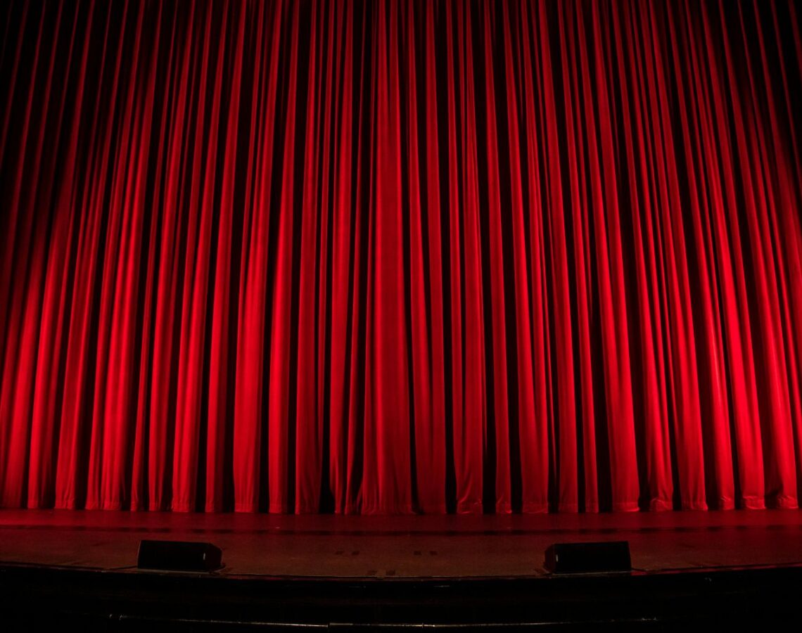 Roter, geschlossener Theater- oder Bühnenvorhang, gleichmäßig beleuchtet auf einer leeren Bühne